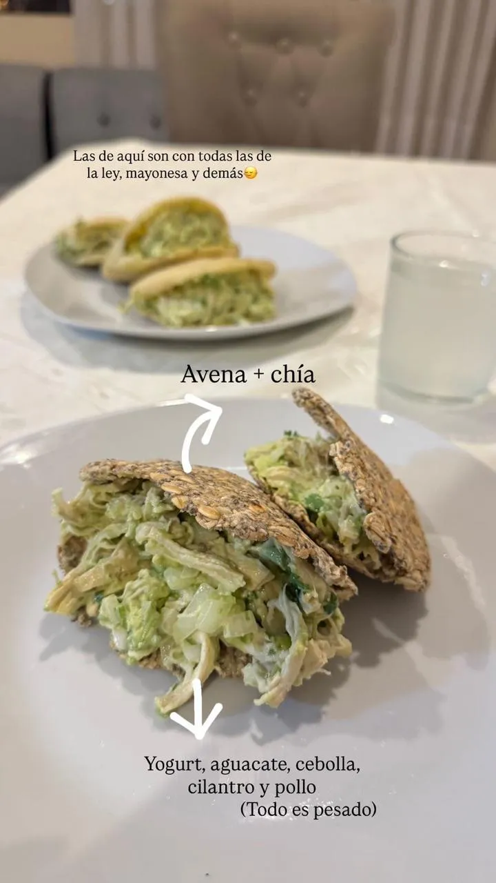 Dos platos servidos en la misma mesa: al fondo el de la familia, adelante el de la clienta, con pollo, aguacate y cebolla sobre galletas de avena y chía.